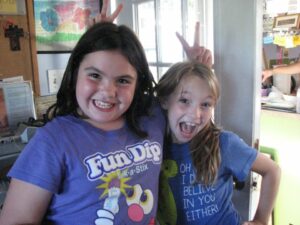 Two girls smiling and giving each other rabbit ears